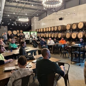 A group of people sitting at tables in front of barrels.