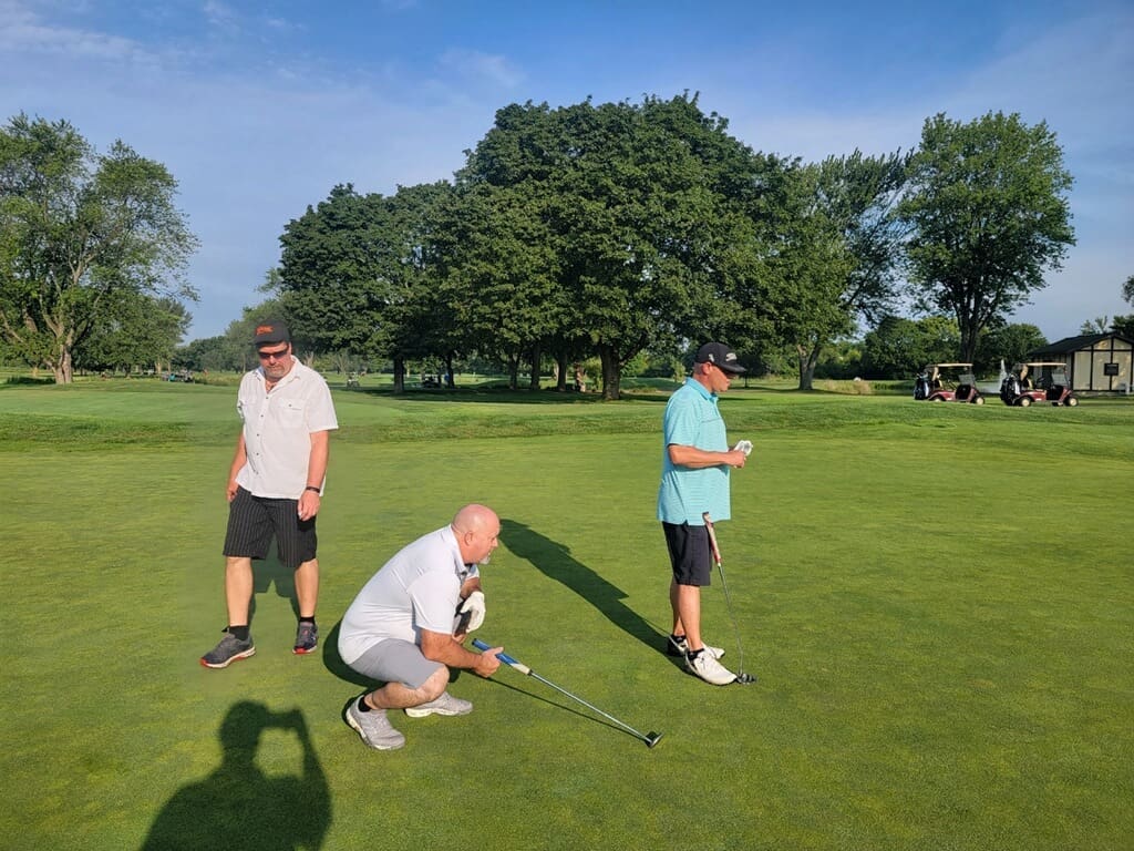 Three men golfing on a green course.