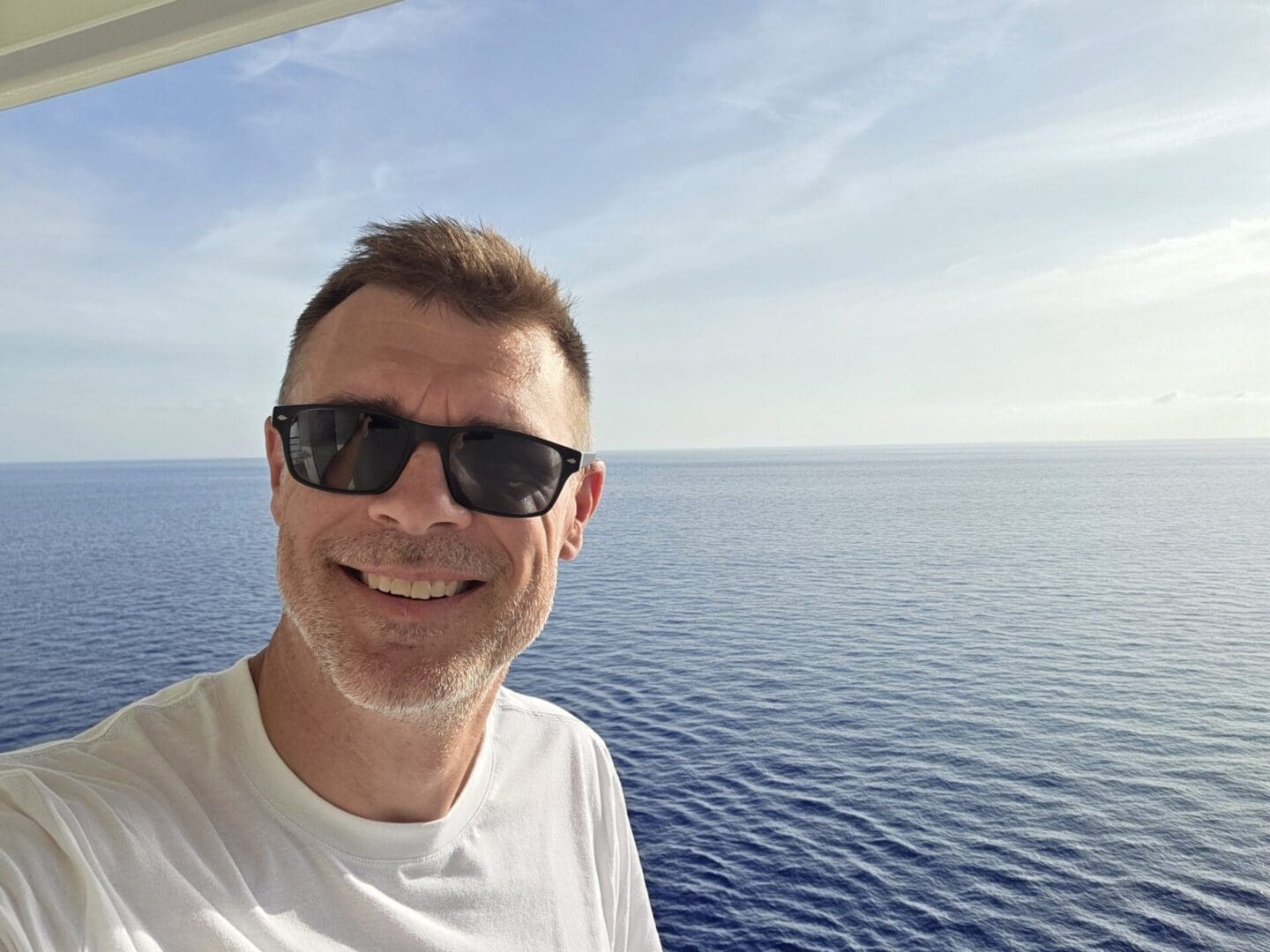 Man smiling in sunglasses by the ocean.