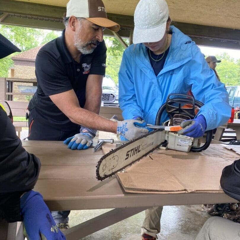 Two people sharpening a chainsaw together